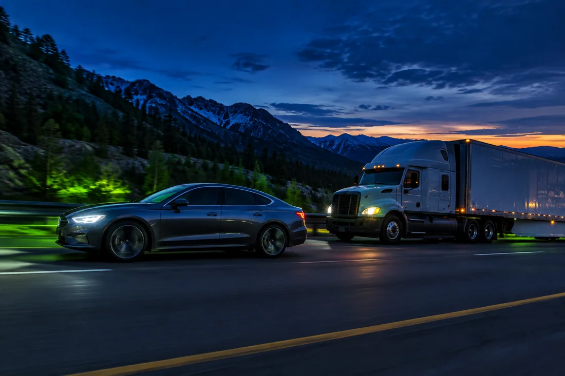 Sedan passing a semi truck on an uphill interstate at dusk